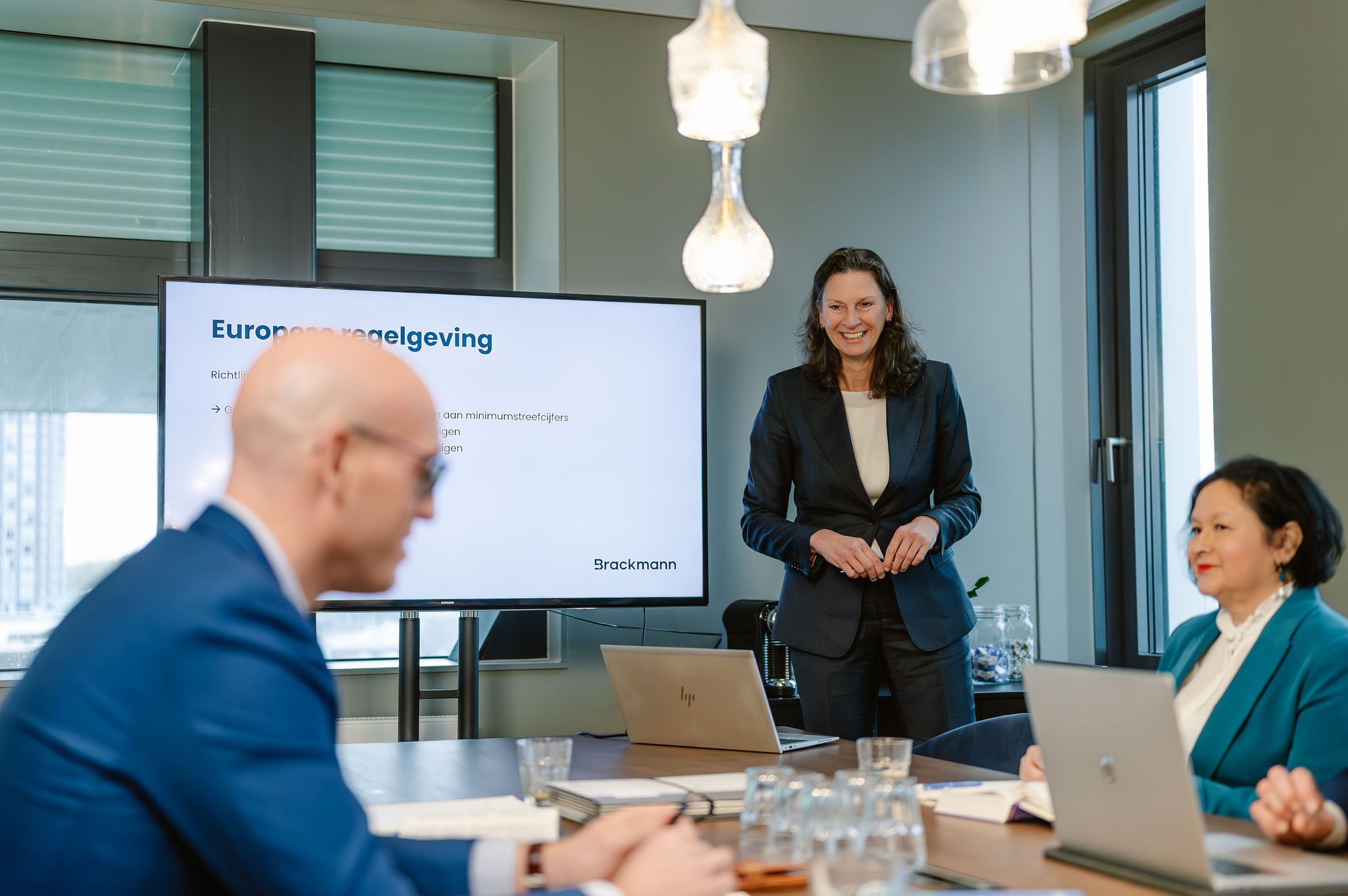 Vergadering met drie mensen waarvan een staand die een presentatie geeft naast een scherm